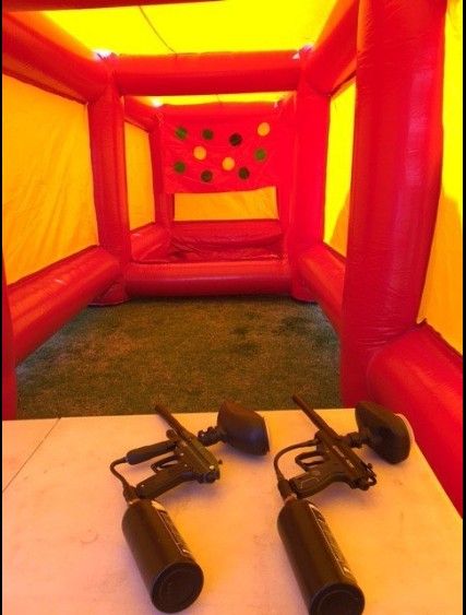 Paintball guns on a table inside a red and yellow inflatable shooting range.