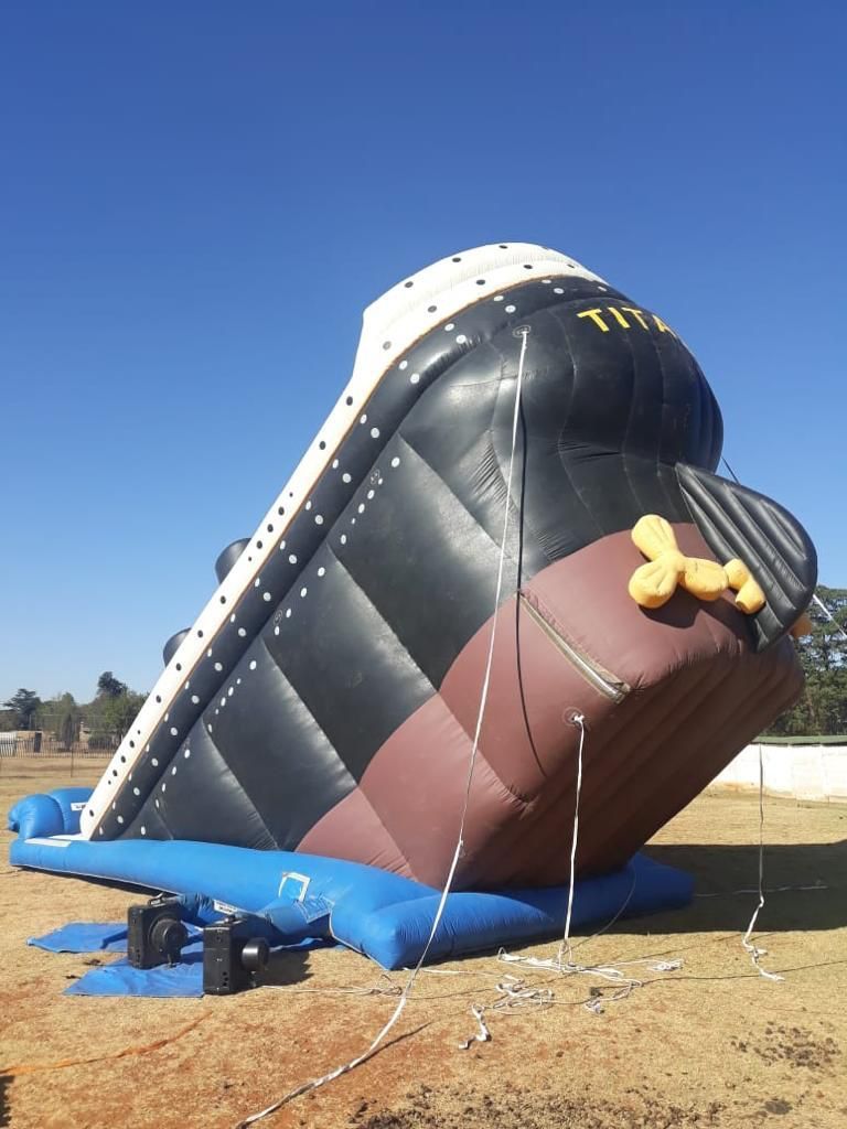 Inflatable Titanic ship, tilted, on a grassy field. Black, brown, and white colors, blue base. 