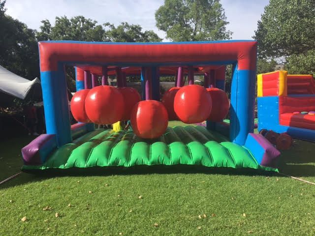 Inflatable obstacle course with red hanging punching bags, green floor, and colorful supports on grass.