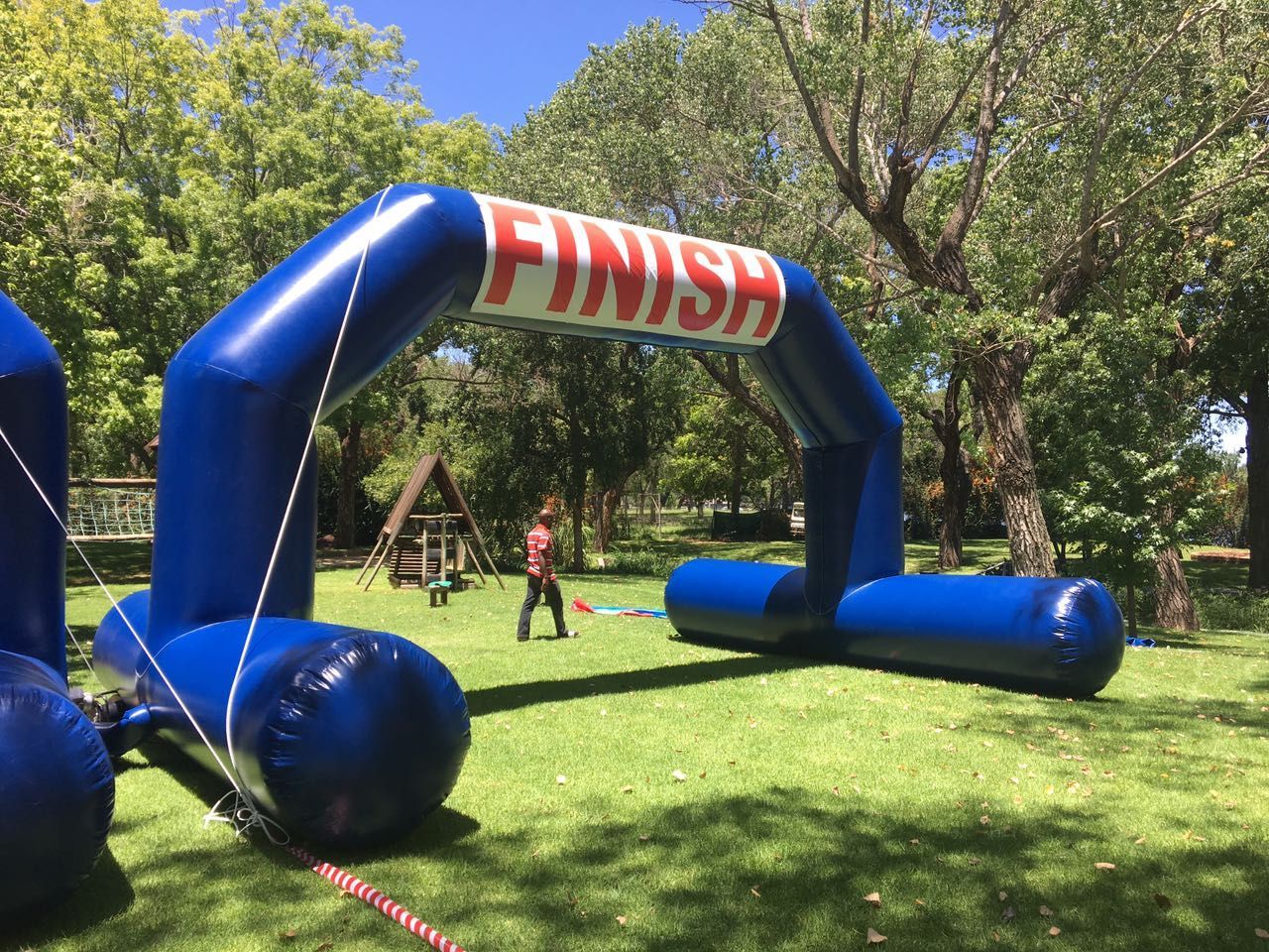 Blue inflatable finish line arch on a grassy field with a person in the background.