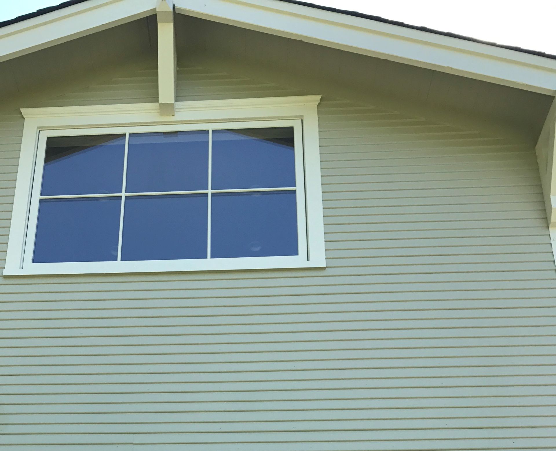 Window with white trim on a green-sided house that has been freshly washed, under a gabled roof.