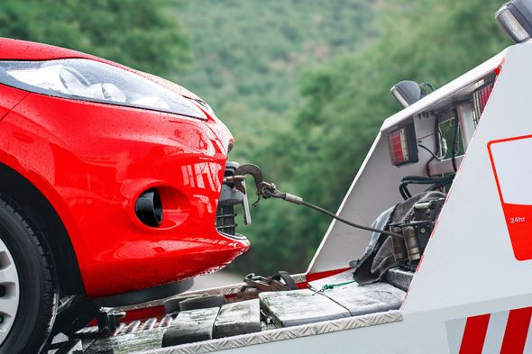Red car being loaded onto a tow truck with a cable, outdoors near greenery