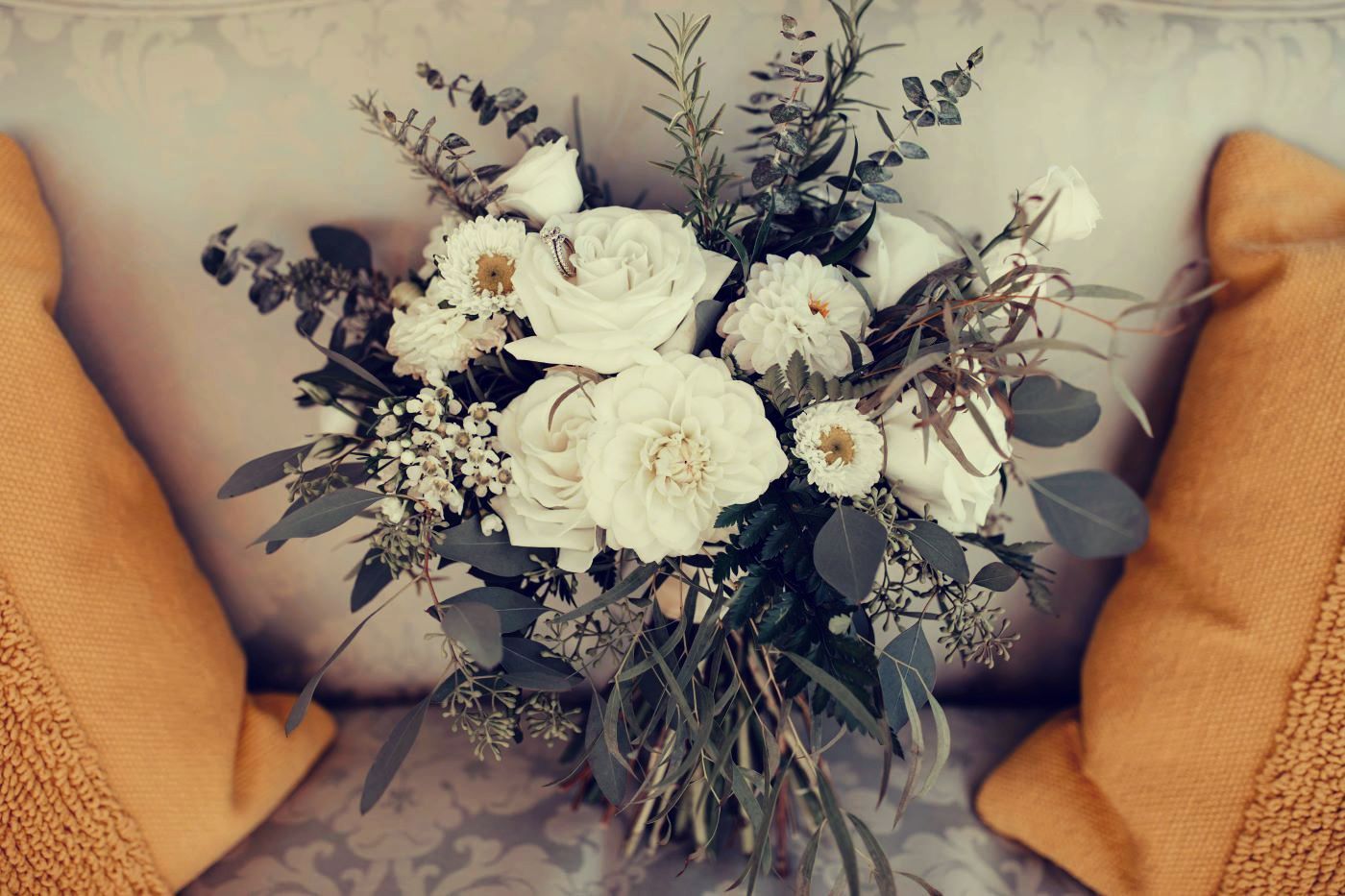 A bouquet of white flowers is sitting on a couch between two pillows.