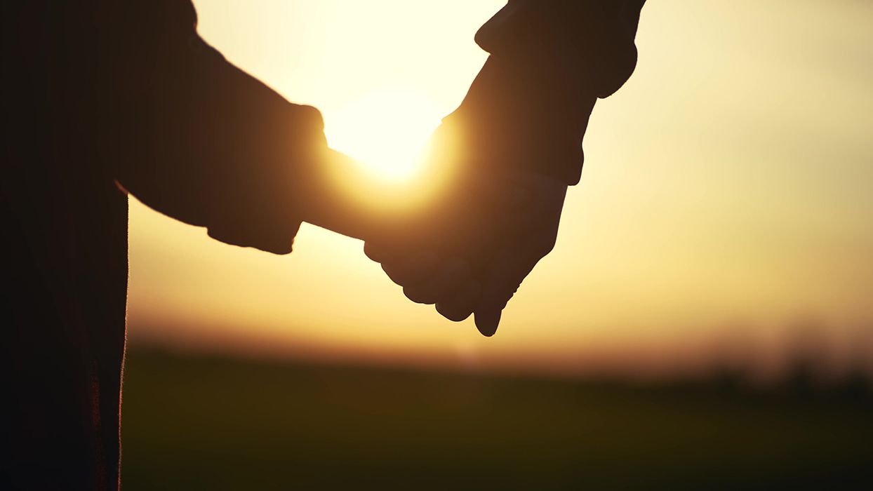 A couple is holding hands in front of the sun at sunset.
