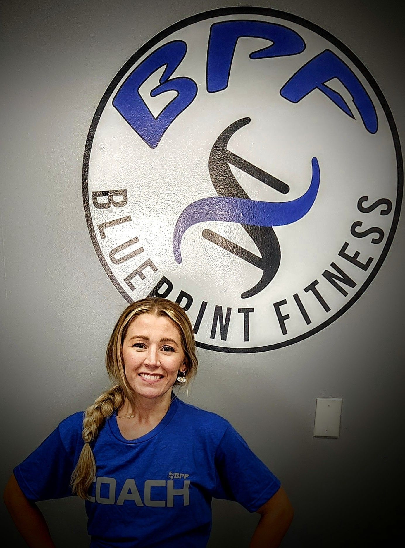 A woman in a blue shirt is standing in front of a blue point fitness logo.