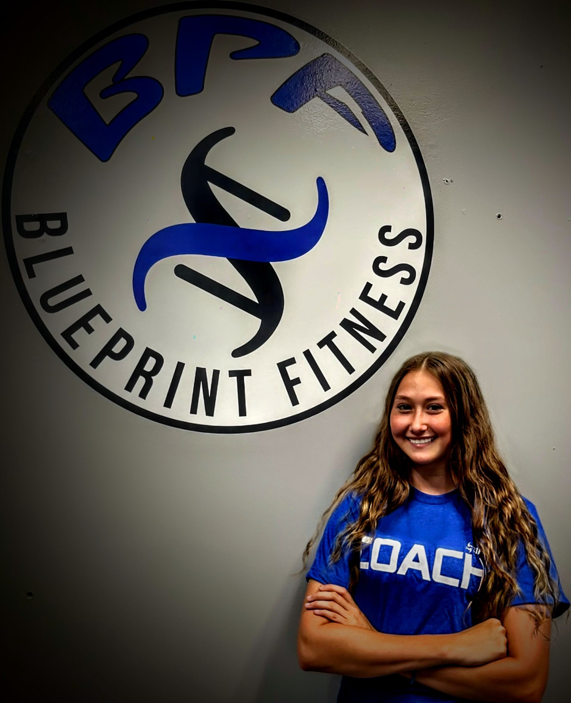 A woman stands in front of a blueprint fitness logo
