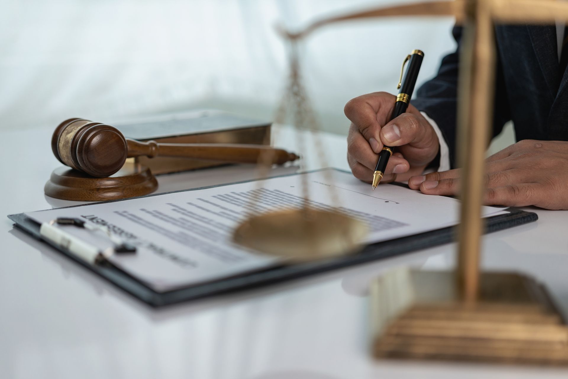 A person in a suit signing a document, with a gavel and scales of justice on the table.