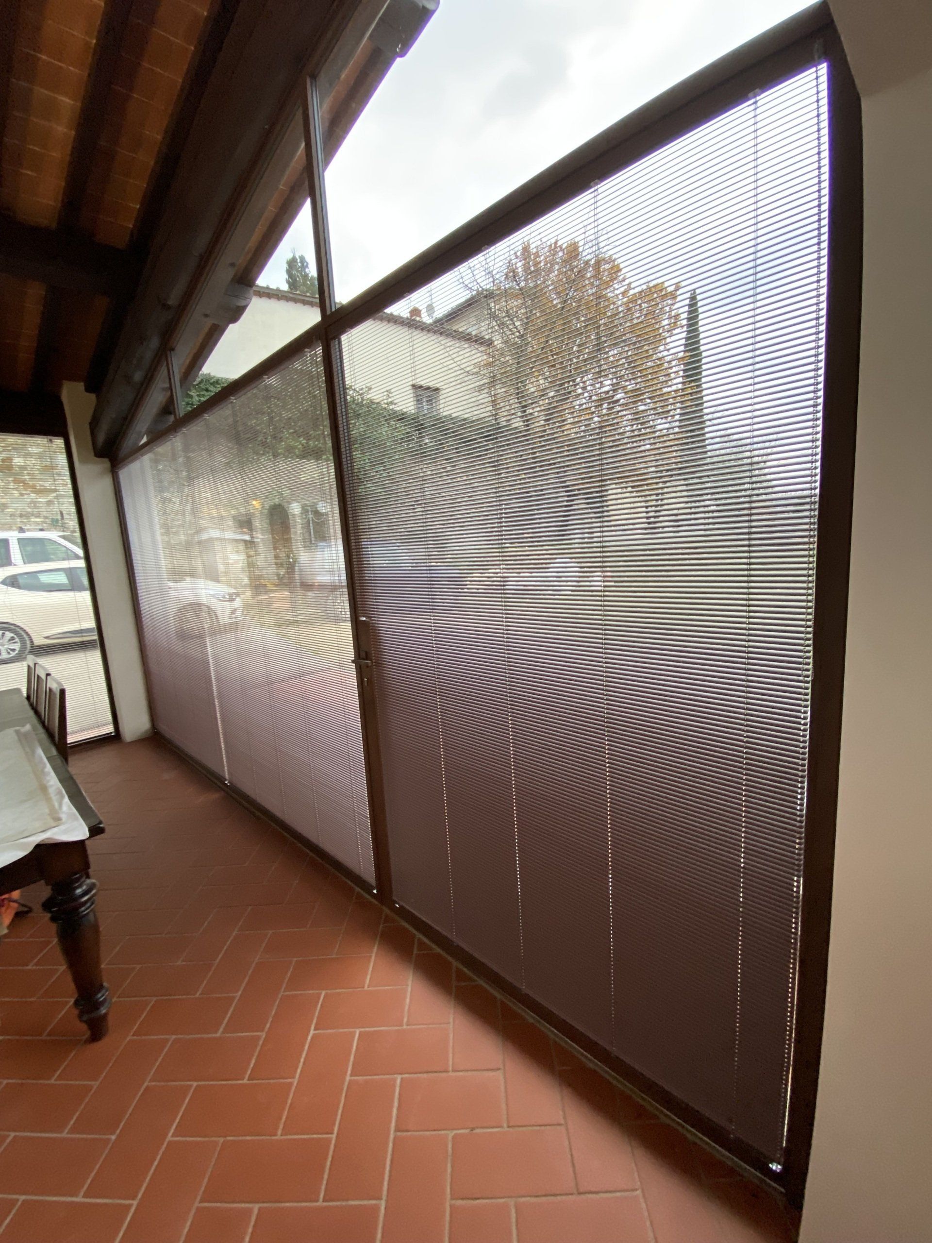 Le tende a rullo marroni coprono un portico finestrato con piastrelle in terracotta.