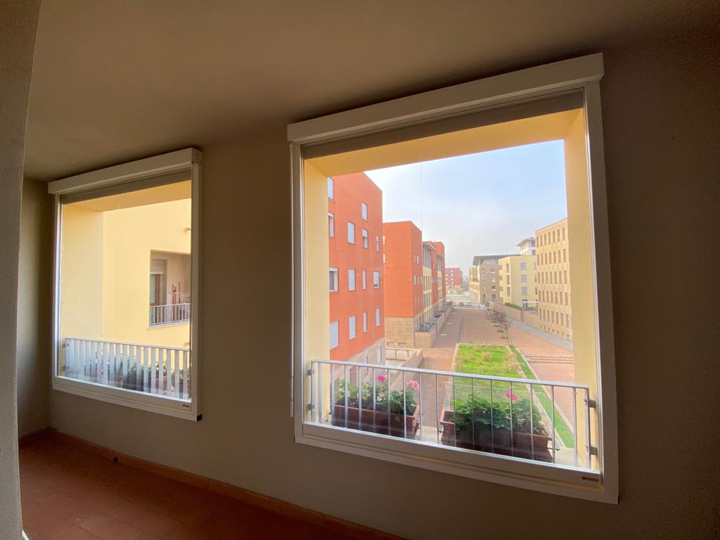 Due finestre si affacciano su un cortile esterno. Edifici nei toni del rosso, del giallo e del beige.