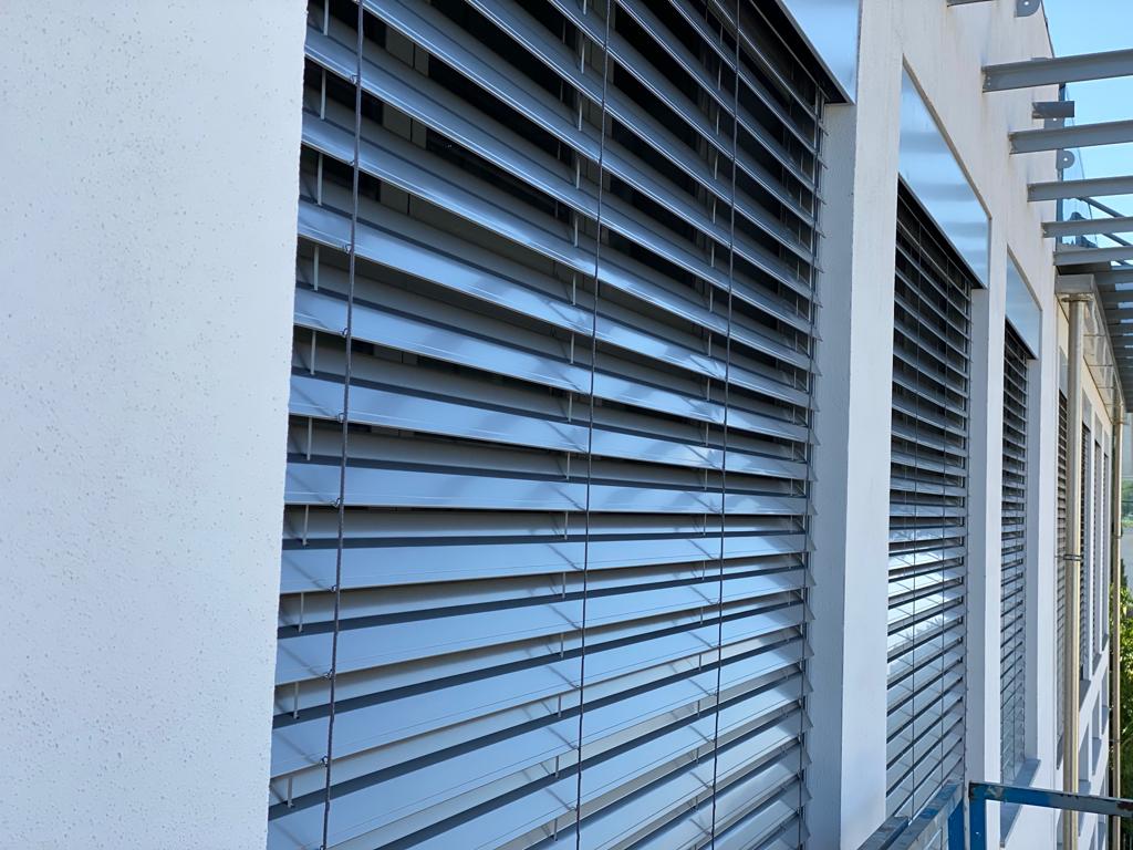 Esterno dell'edificio con persiane metalliche chiuse che coprono le finestre.