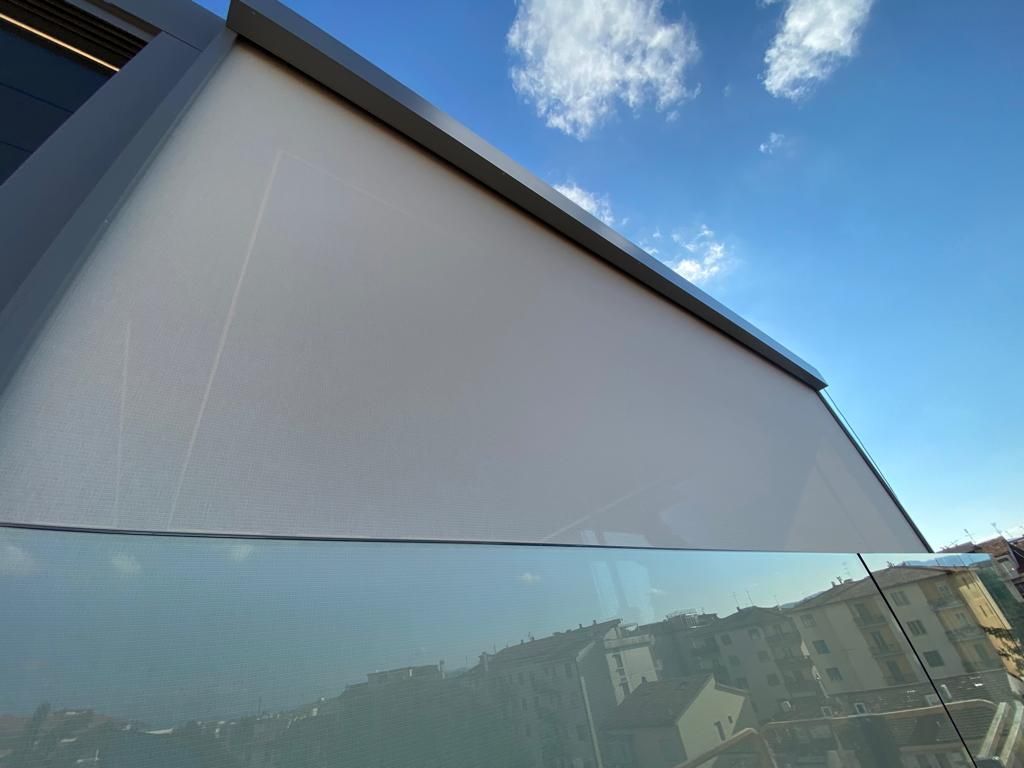 Un grande ombrellone bianco su un edificio moderno riflette il cielo e la città sottostante. Cielo azzurro con nuvole.