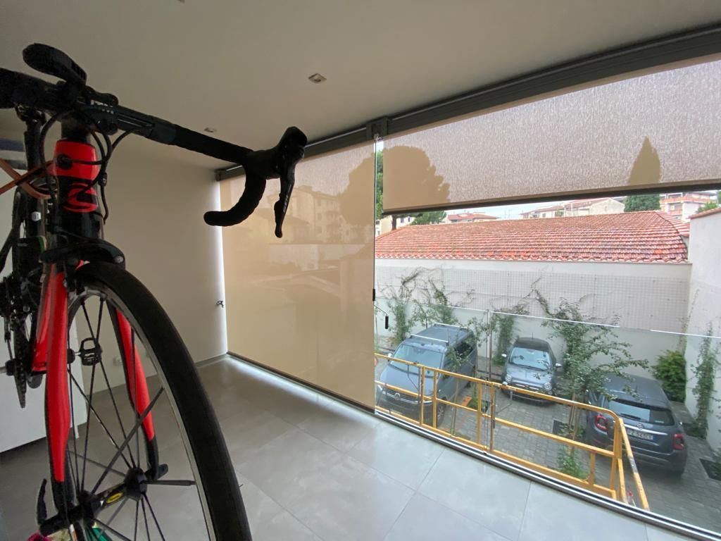 Una bici da strada è appesa vicino a una finestra con vista sulle auto e sul tetto di tegole rosse.