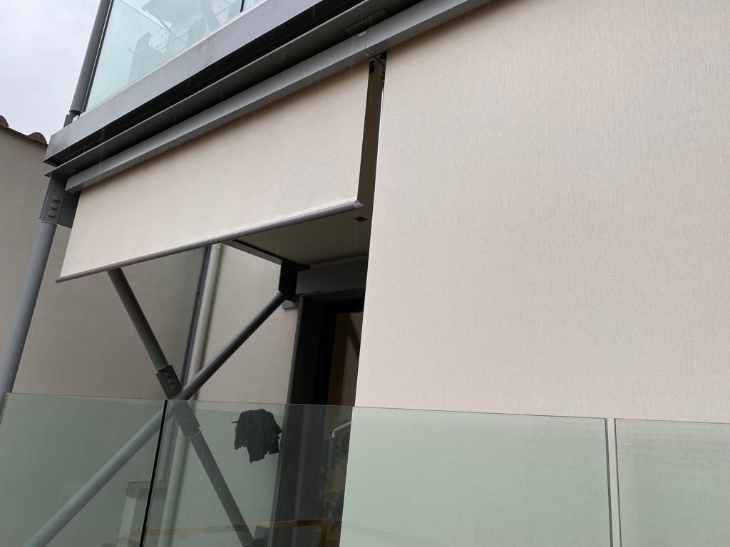 Tenda da sole retrattile beige parzialmente estesa su un balcone in vetro.