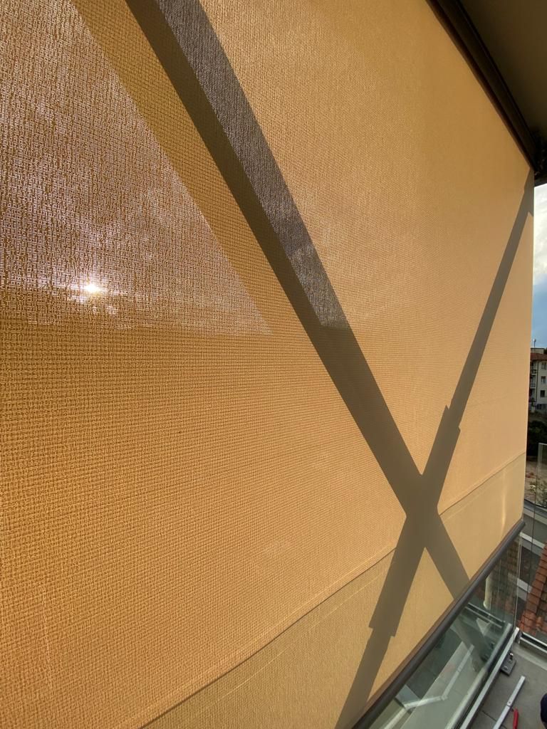 Tenda parasole in rete beige sulla facciata di un edificio; le ombre delle travi trasversali creano un motivo a X.