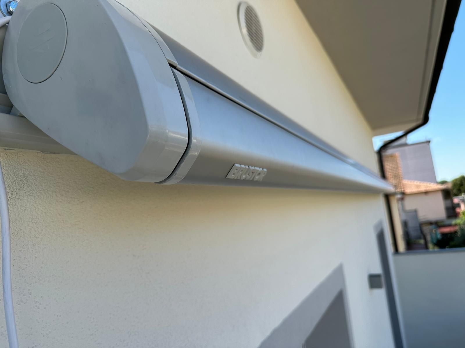 Tenda da sole retrattile grigia montata sulla facciata di un edificio di colore chiaro, sotto un cielo azzurro e terso.