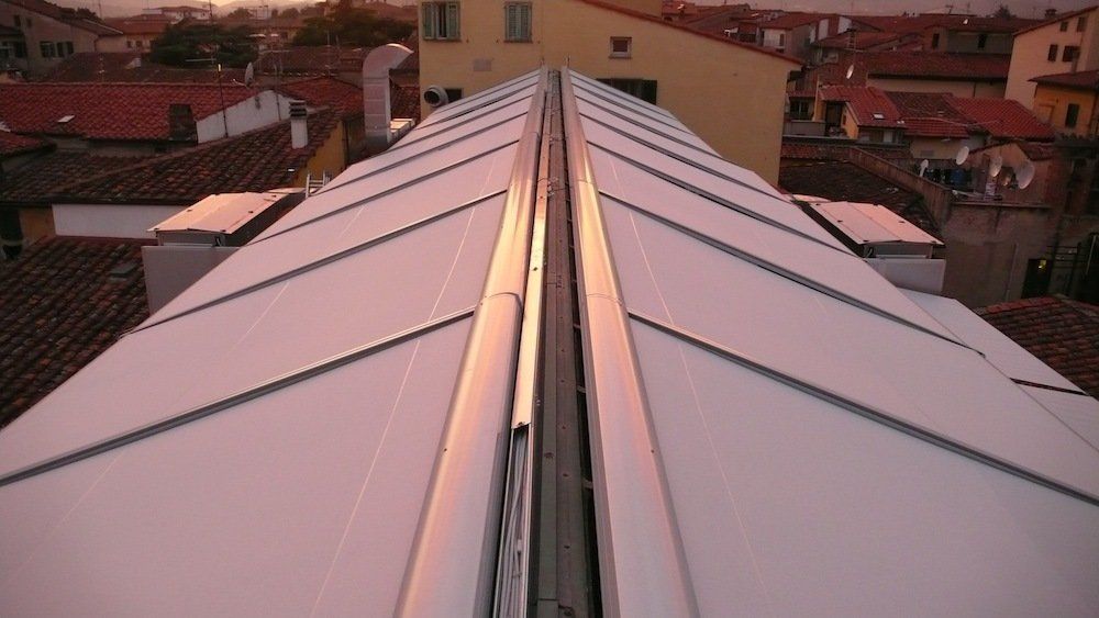 Vista dall'alto di un tetto bianco e spigoloso con bordi metallici, che riflette la luce ambientale sui tetti della città .