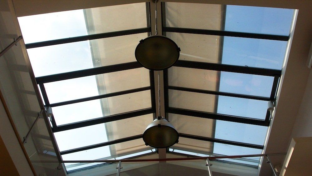 Lucernario con griglia di pannelli di vetro, lampadari sospesi e scorci del cielo azzurro soprastante.