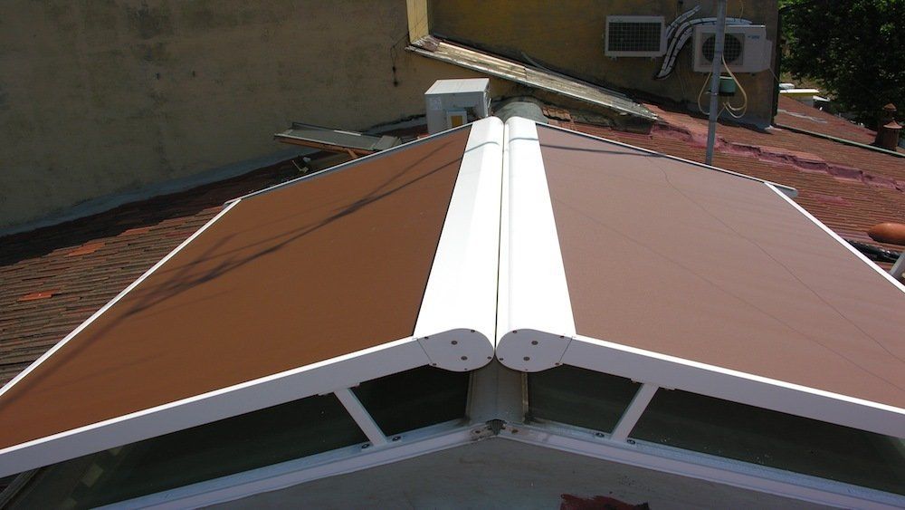 Tenda da sole marrone sopra una finestra sul tetto. Telaio bianco e tetto scuro sotto.
