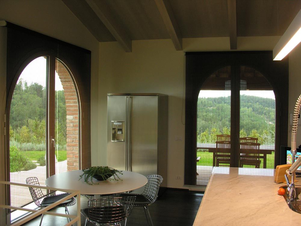 Cucina con tavolo rotondo, frigorifero in acciaio inox e finestra ad arco con vista sul giardino.
