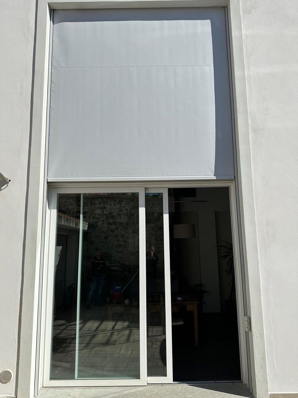 Porte scorrevoli in vetro con tenda esterna bianca abbassata, inserite in una parete esterna bianca.