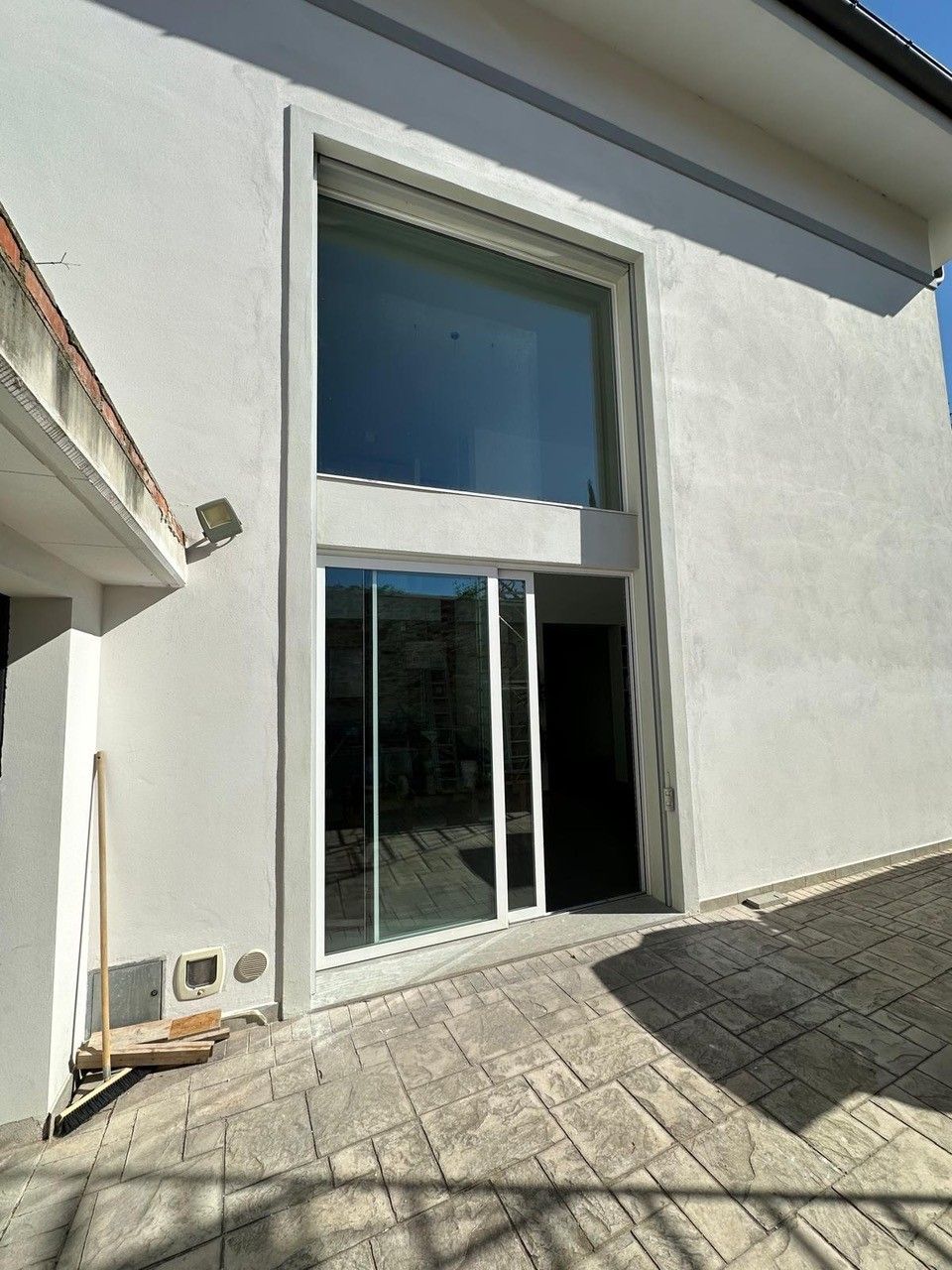 Vista esterna di una moderna casa bianca con ampie finestre. Porte scorrevoli in vetro conducono all'interno.