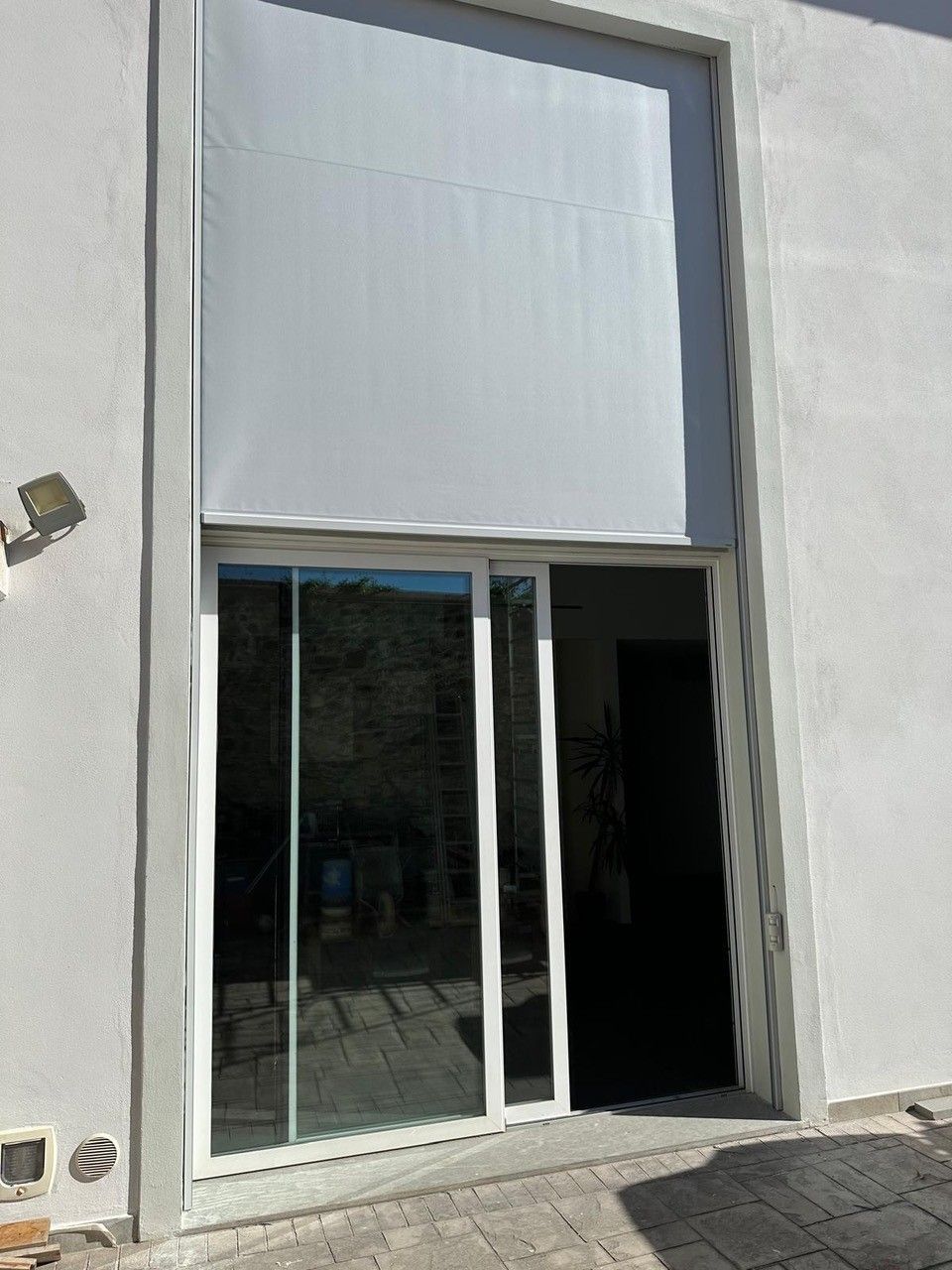 Tenda da sole retrattile bianca sopra la porta scorrevole in vetro di un edificio di colore chiaro.