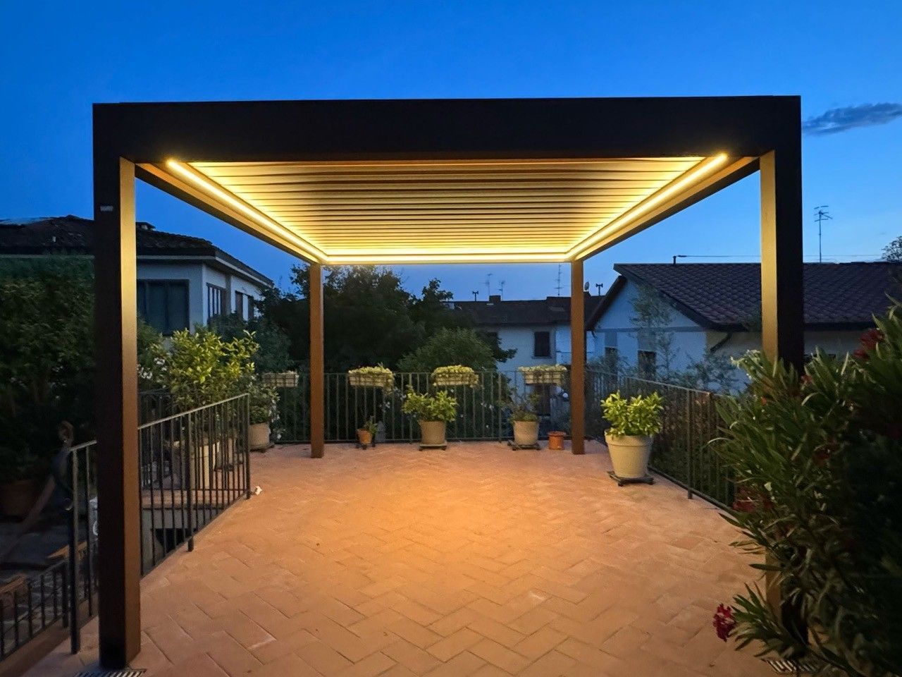 Pergola con soffitto illuminato, su un patio in mattoni al tramonto.