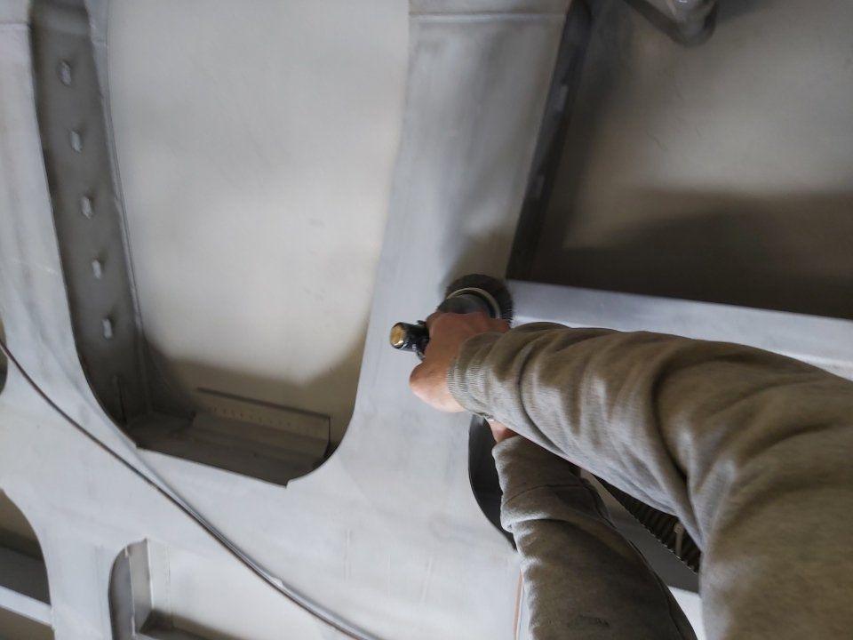 Persona che utilizza un utensile elettrico portatile su un pannello a muro grigio chiaro con aperture.