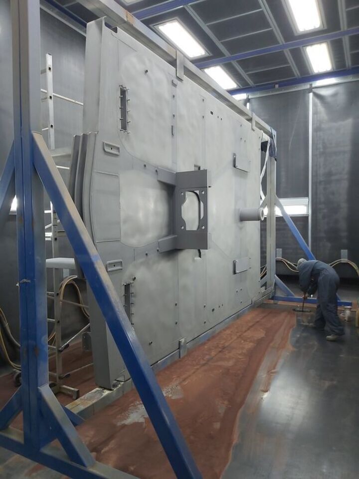 Grande macchinario industriale in una fabbrica, con un operaio che lo ispeziona sulla destra.