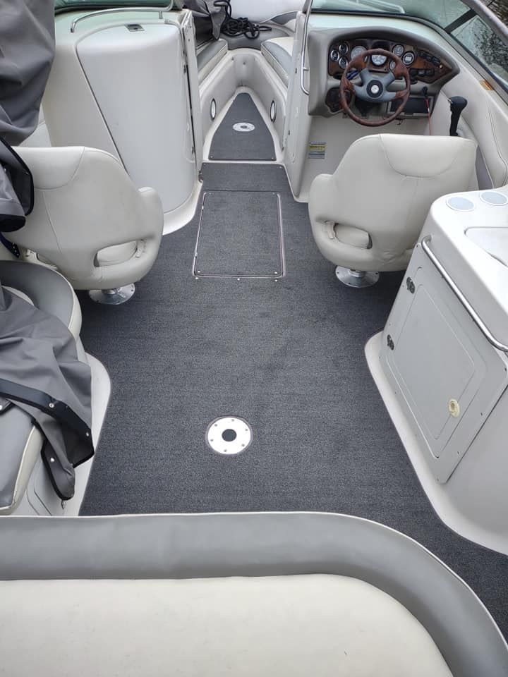 Boat cockpit with gray carpet, white seats, and a steering wheel at the helm