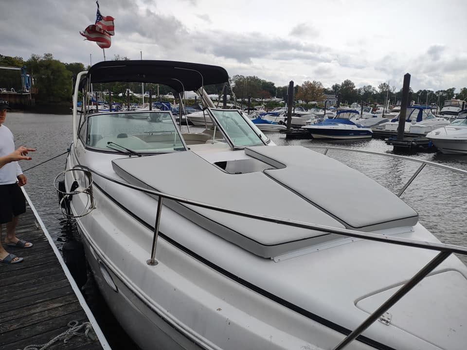 White cabin cruiser docked at a marina, with a black canopy and closed bow covers.