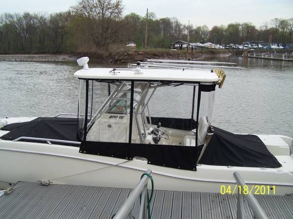 Boat with black canopy on calm water, viewed from a dock with trees in the background.