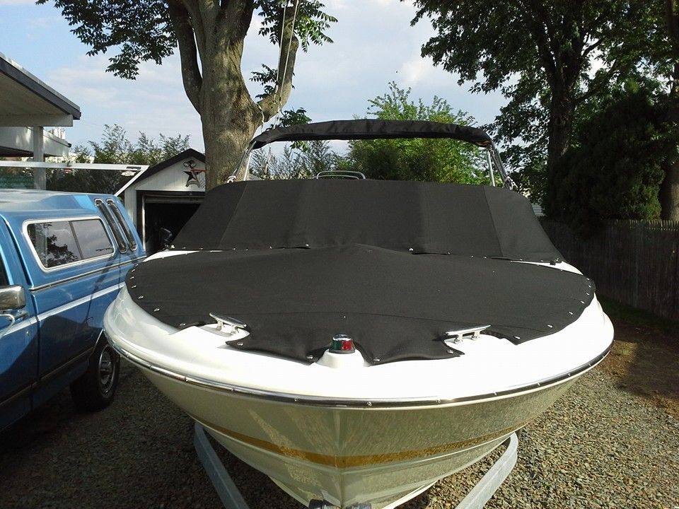 Front view of a white boat with a black cover parked in a gravel driveway beside a blue van.