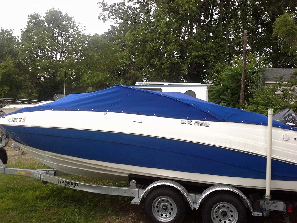Blue and white speedboat on a trailer, covered with a blue tarp, parked outdoors among trees