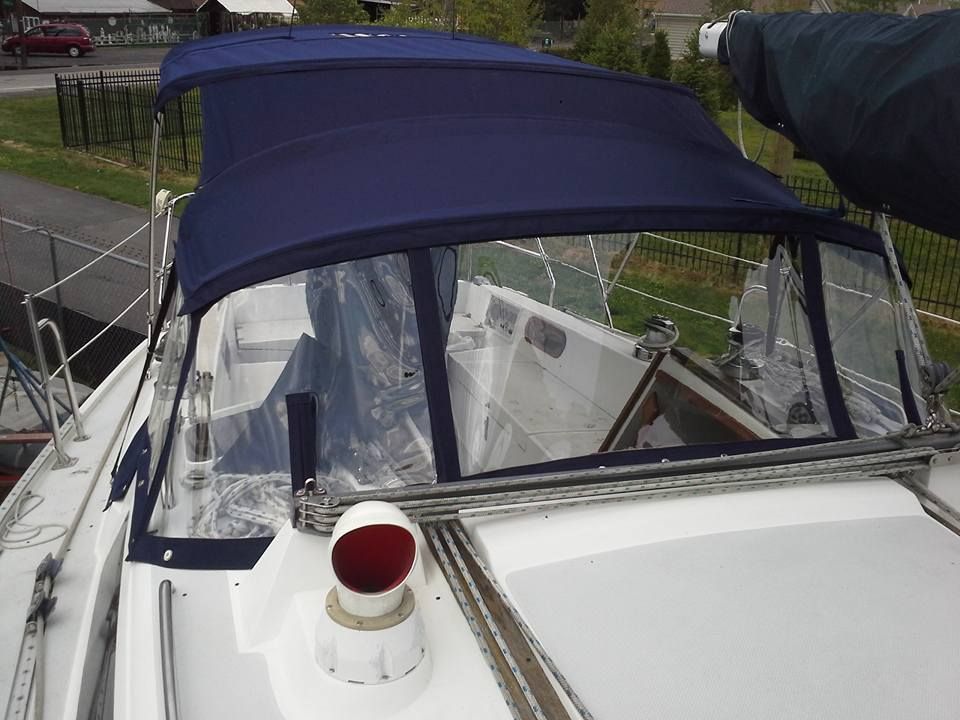 White sailboat with a dark blue canopy docked outdoors, showing the cockpit and windshield