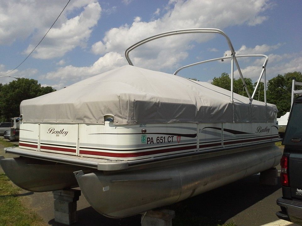 Covered pontoon boat on a trailer parked outdoors under a cloudy sky