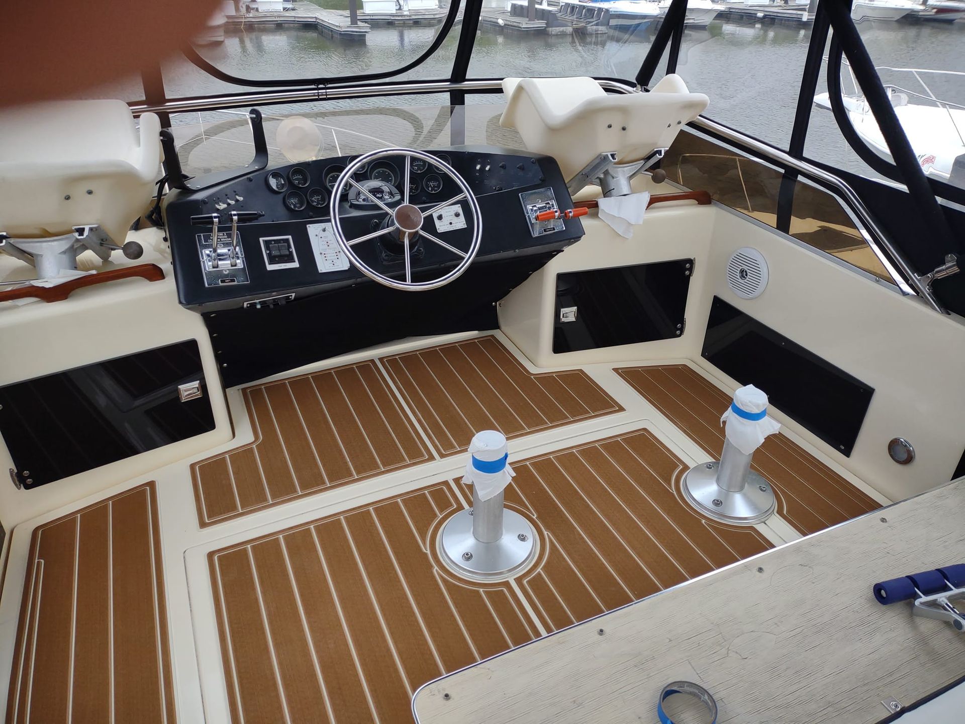 Boat cockpit with black helm, white seats, and tan teak-style flooring facing the water