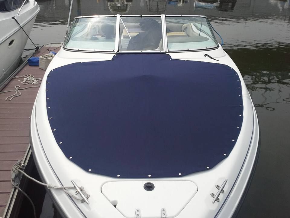 White boat with a dark blue cover docked at a marina, viewed from the front.