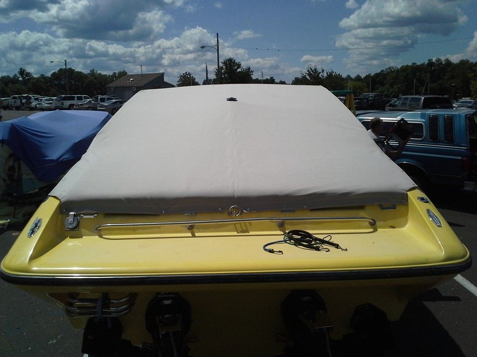 Yellow boat with a beige cover on a trailer, viewed from the rear under a cloudy sky