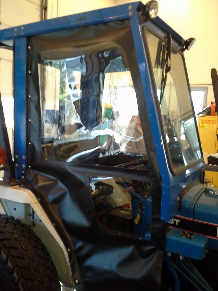 Blue tractor cab with a broken side window and torn black door panel inside a garage