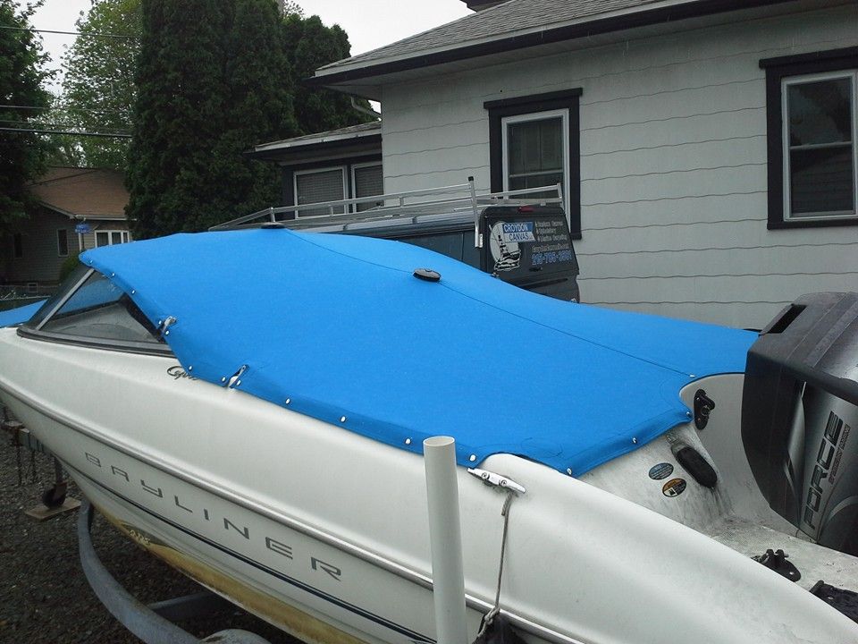 White speedboat with a blue cover parked beside a house.