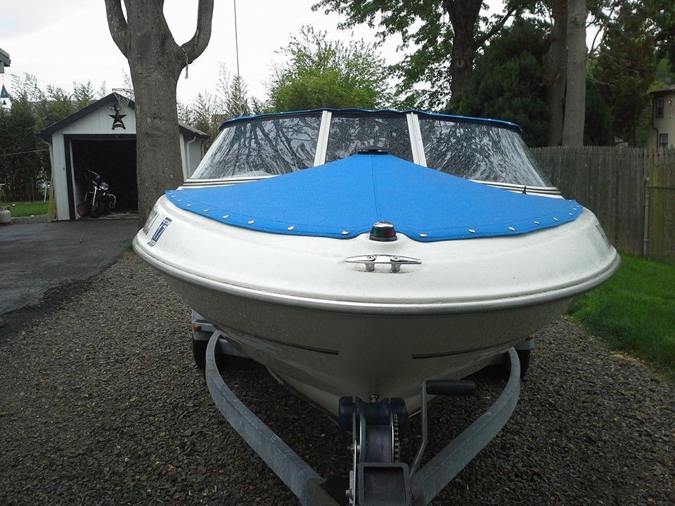 White and blue speedboat on a trailer in a driveway, with a garage and trees in the background
