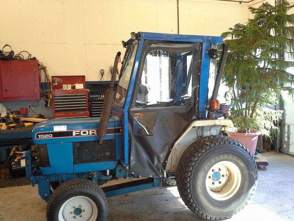 Blue Ford tractor in a garage, with a covered cab and large rear tire.