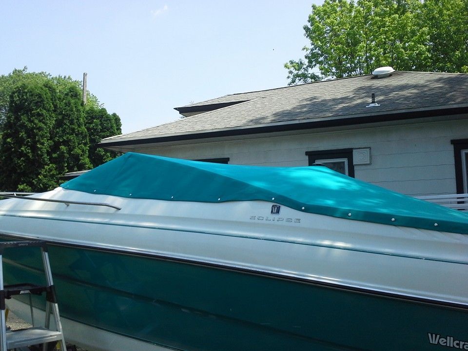 Teal boat on a trailer parked beside a white house under a sunny sky