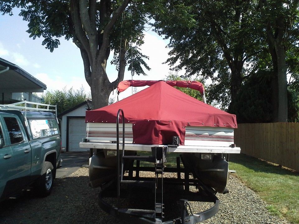 Red canopy on a boat trailer in a driveway beside parked vehicles and trees