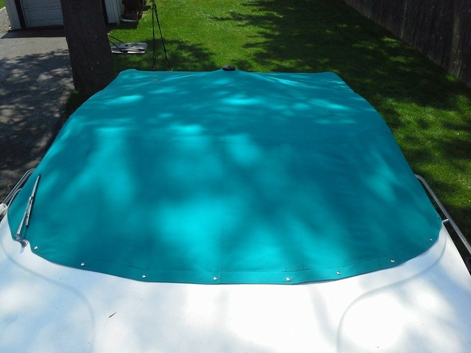 Blue tarp covering a white boat outdoors on grass and pavement