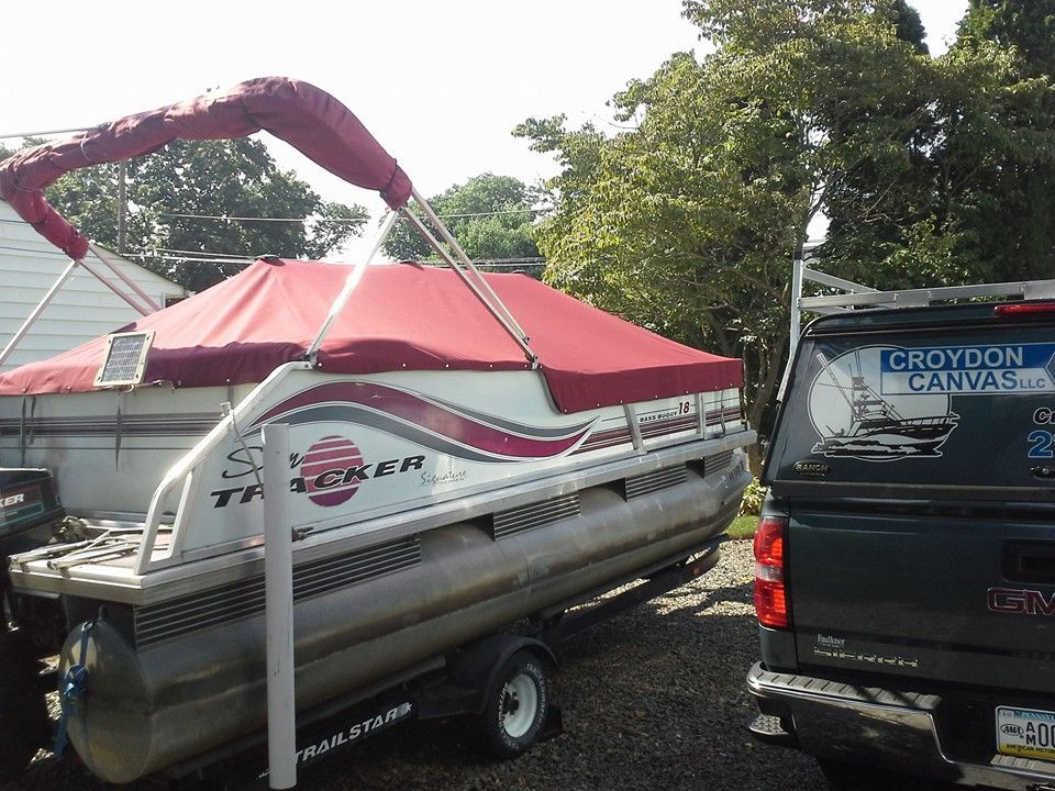 Pontoon boat on a trailer with a red canopy beside a black Croydon Canvas van outdoors