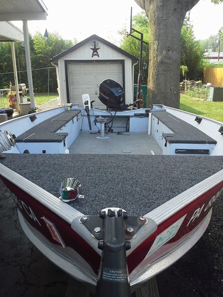View from a boat bow toward a small garage, with rod holders, a trolling motor, and an outboard motor on deck