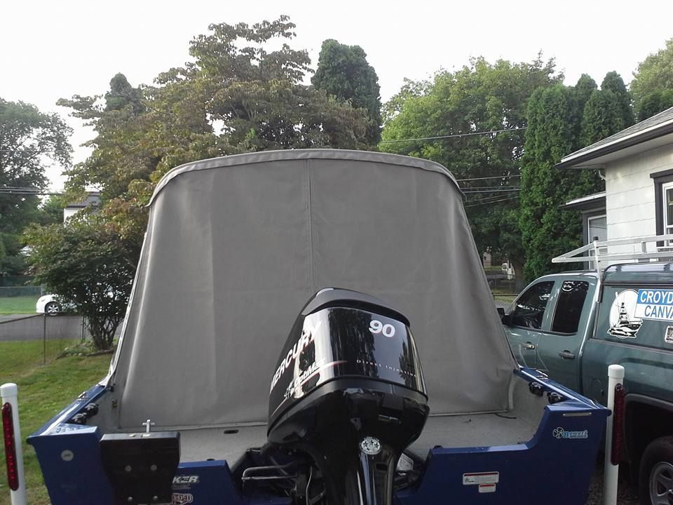 Blue boat with gray cover and black outboard motor parked outdoors near trees and a house