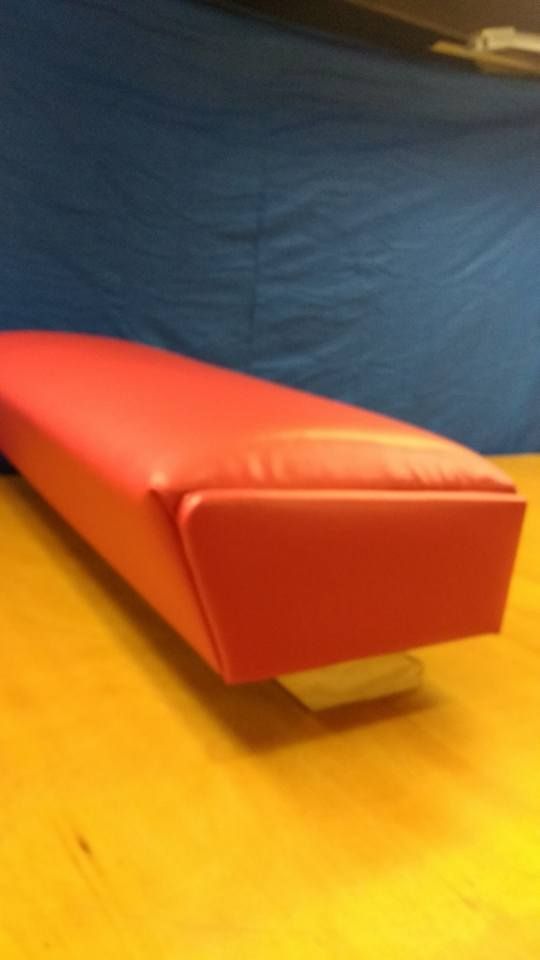 Red padded bench or gym apparatus on a wooden floor with a blue backdrop